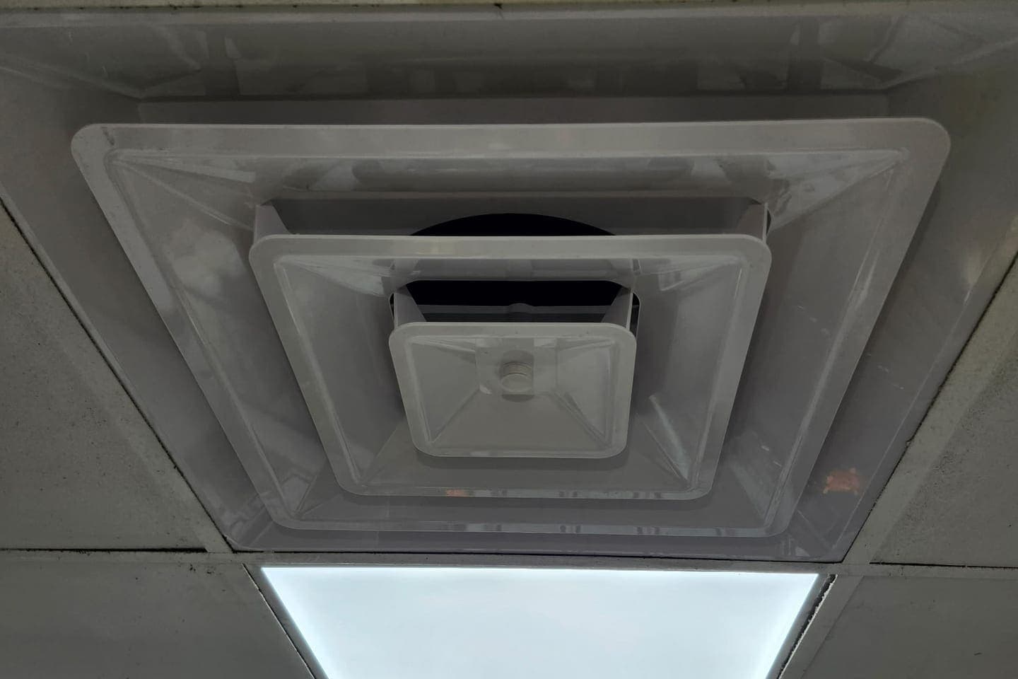 A ceiling return grille beside a light panel.