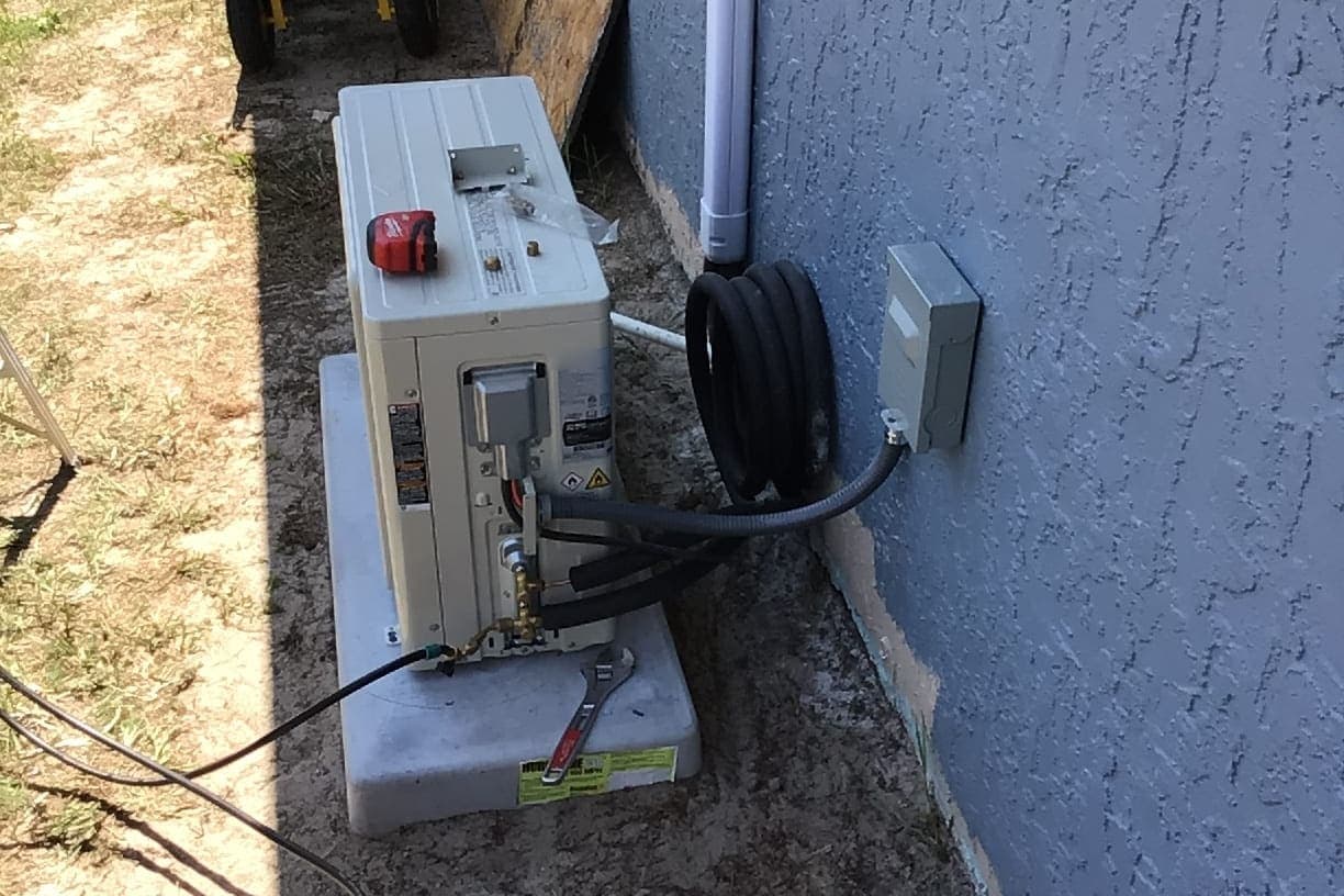 A ductless mini-split outdoor unit being set beside a stucco wall.