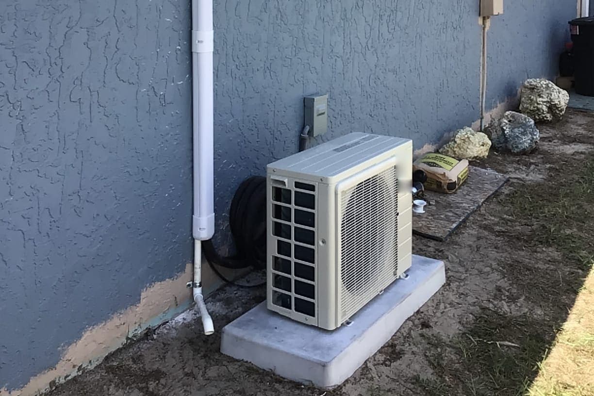 A ductless outdoor unit beside a window and a gutter downspout.