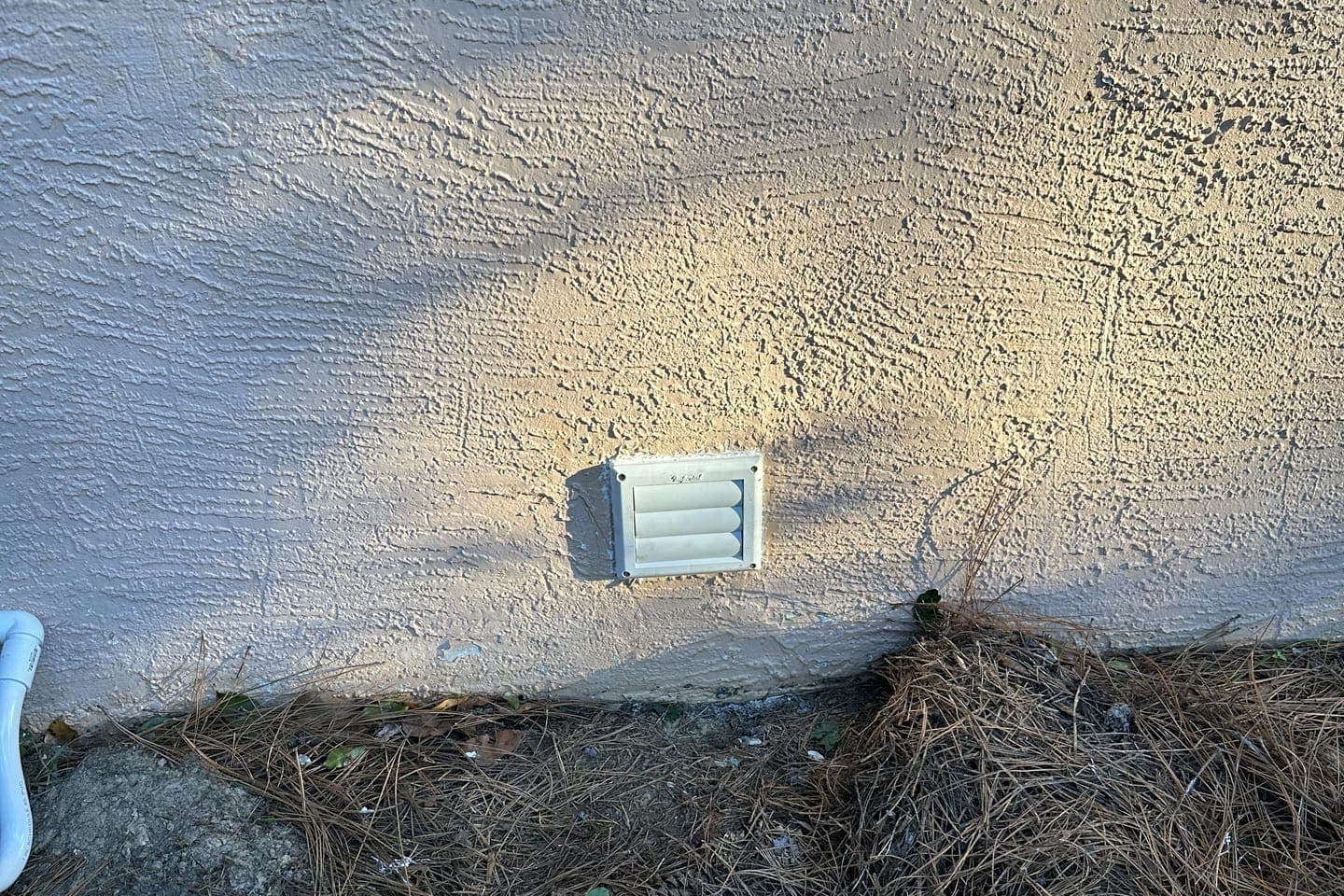 An exterior wall vent cover with pine straw below it in Spring Hill, FL.