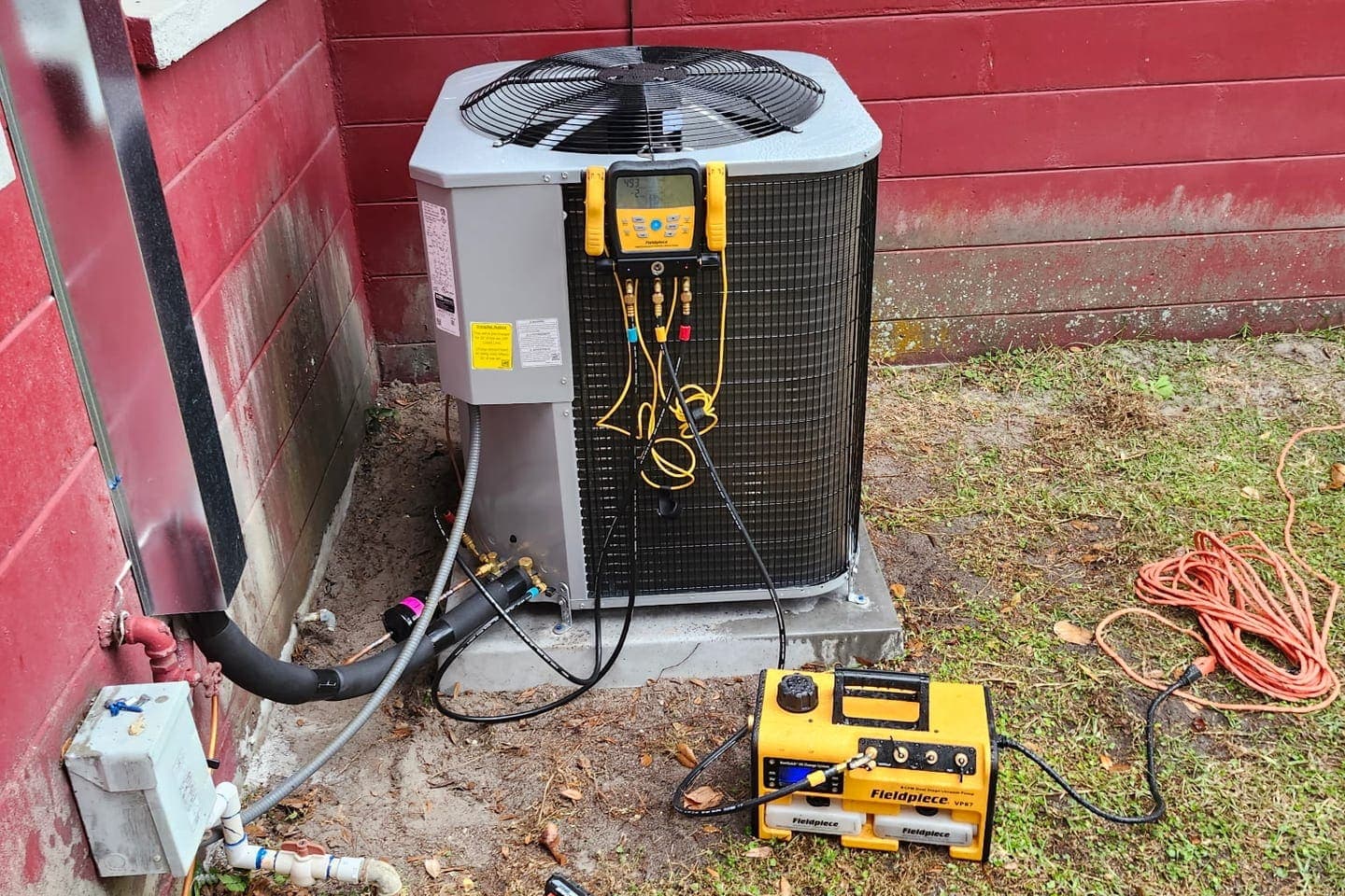 An outdoor condenser hooked up to a gauge manifold and vacuum pump during a service call.