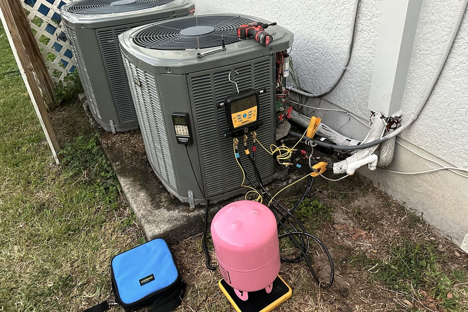 An outdoor condenser with a pink refrigerant cylinder and a recovery machine beside it in Spring Hill, FL.
