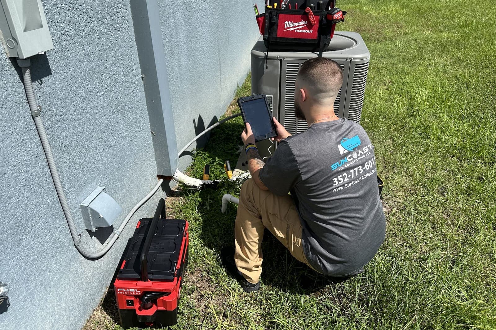 A SunCoast technician checking readings on a tablet beside an outdoor condenser in Spring Hill, FL.