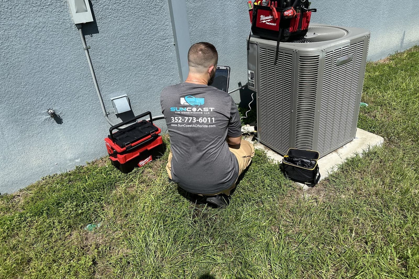 A SunCoast technician crouched at an outdoor condenser during a service visit in Spring Hill, FL.