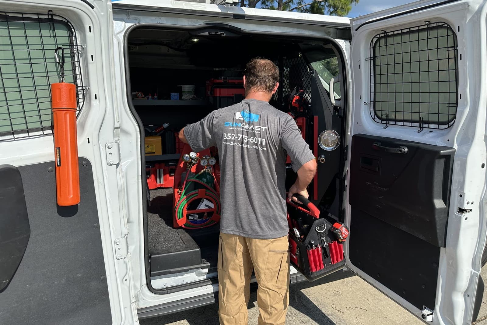 A SunCoast technician at the open back doors of the van, with tool cases racked inside in Spring Hill, FL.