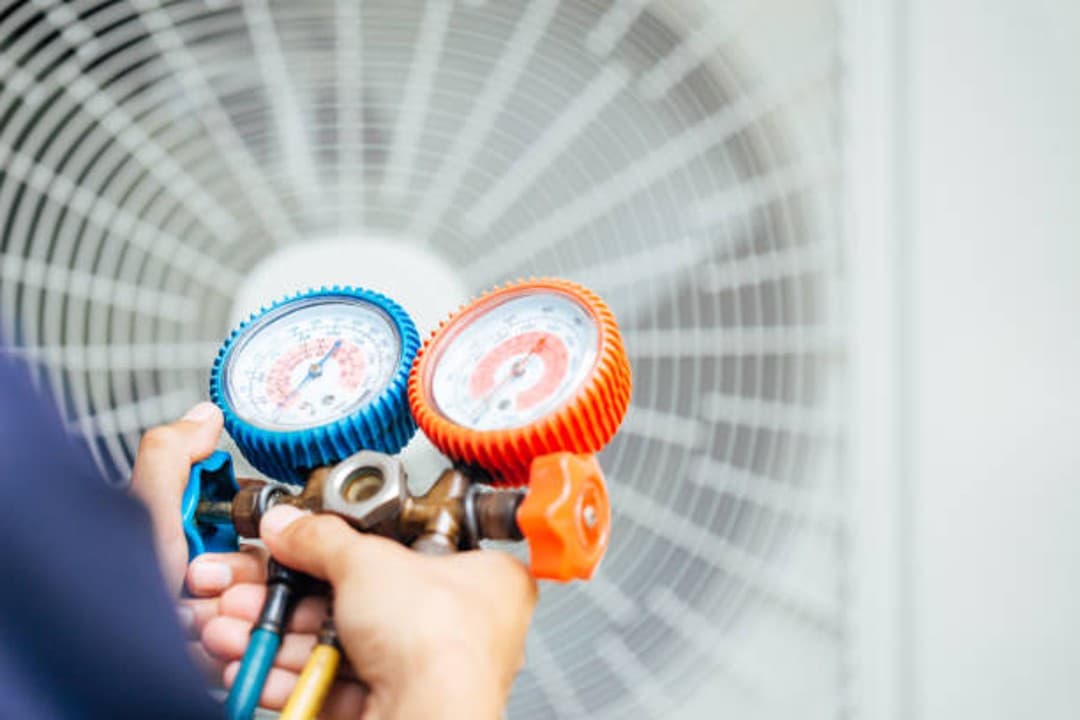 Technician holding a refrigerant manifold gauge set in front of a condenser fan