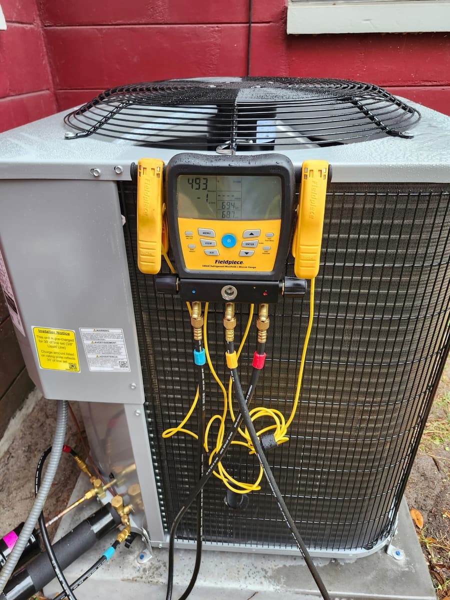 A digital gauge manifold with yellow hoses clamped to a condenser.