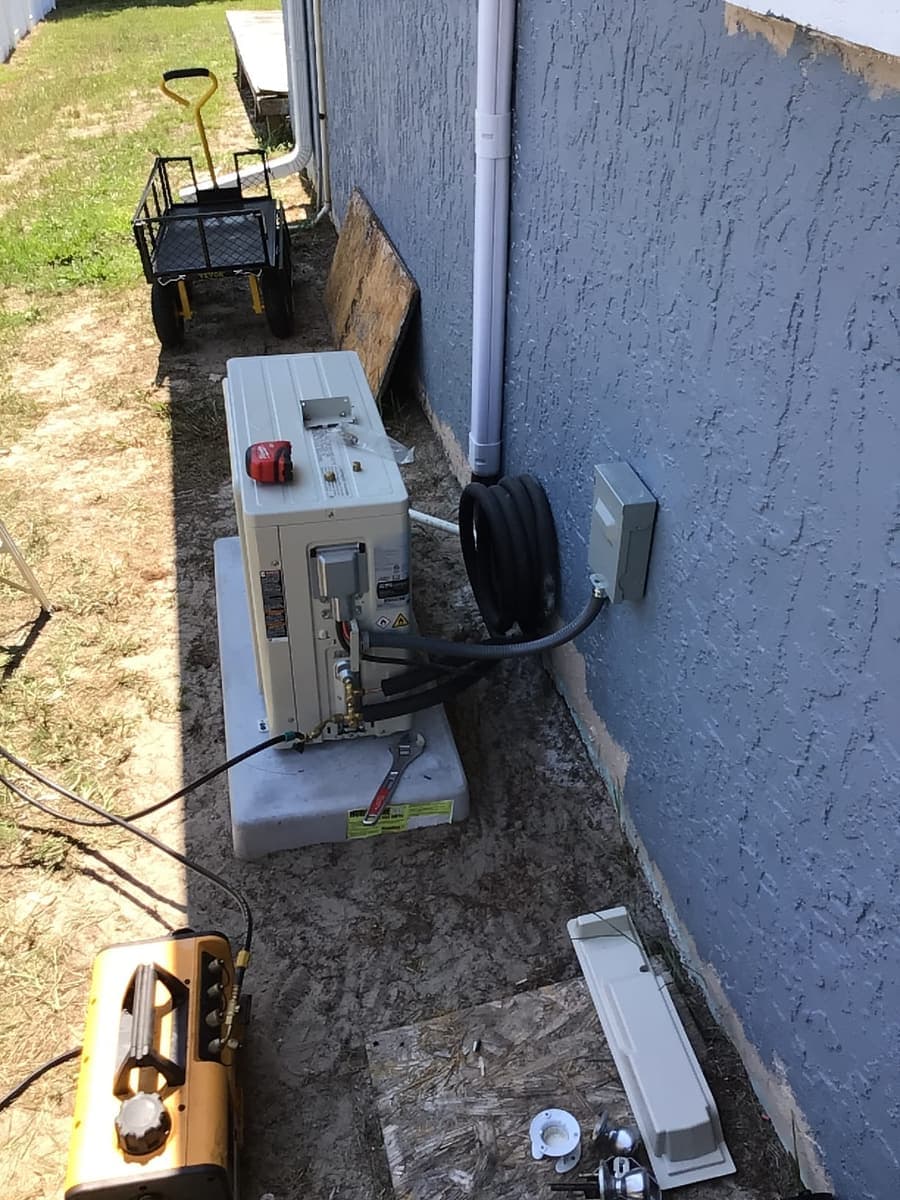 A ductless mini-split outdoor unit being set beside a stucco wall.