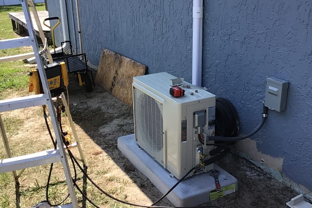 A ductless outdoor unit on a pad with its line set run to the wall.