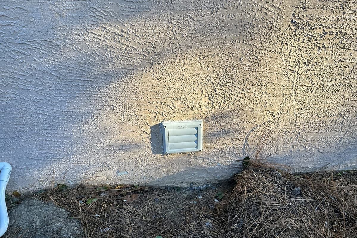 An exterior wall vent cover with pine straw below it in Spring Hill, FL.