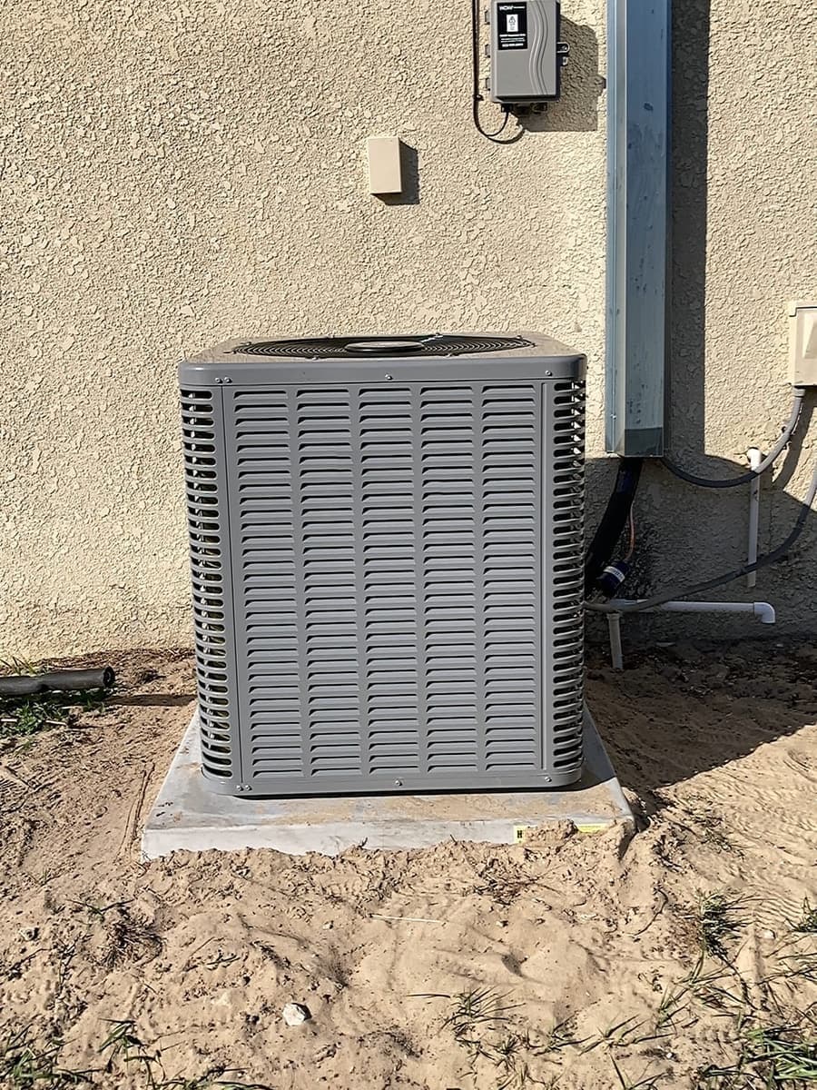 A gray outdoor condenser on a pad beside a stucco wall.