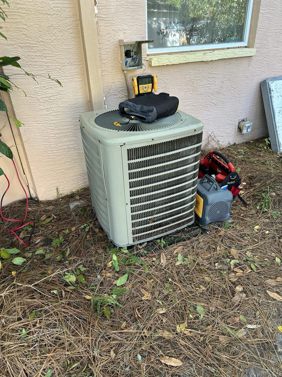 A green outdoor condenser with a vacuum pump and gauge tools beside it in Spring Hill, FL.