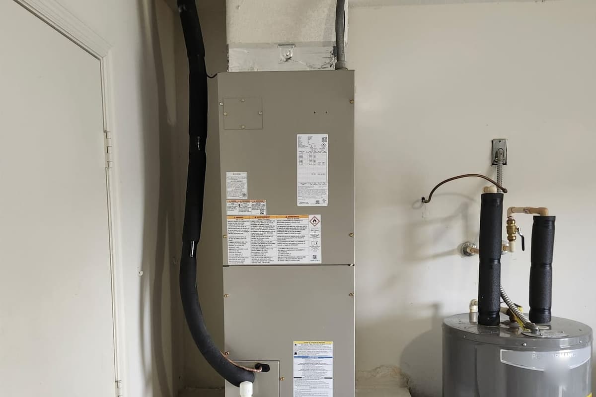 An indoor air handler with its condensate line, beside a water heater.