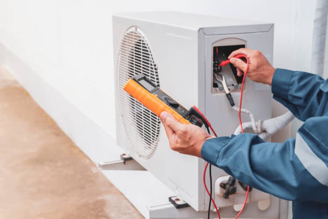 Technician testing the wiring of an outdoor mini-split unit with a multimeter