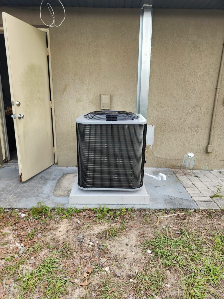 A new outdoor air conditioner condenser on a concrete pad beside a door.