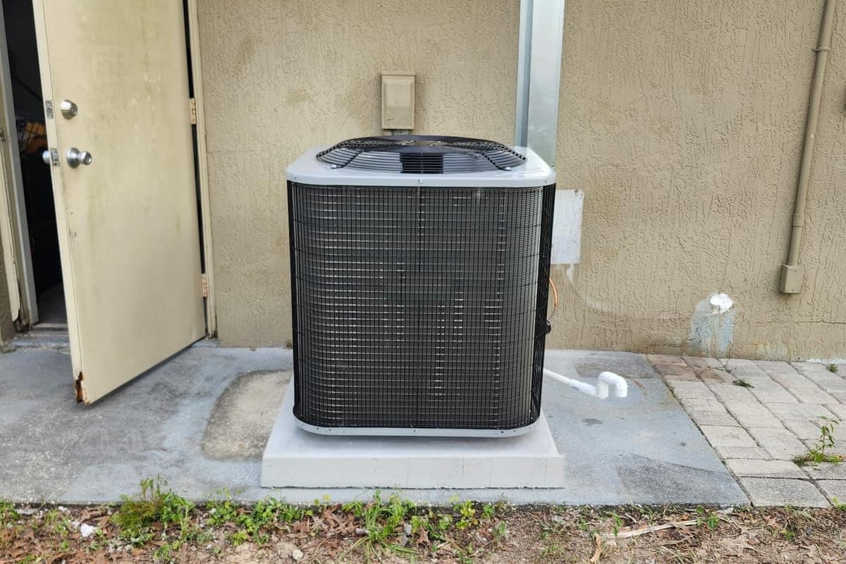 A new outdoor air conditioner condenser on a concrete pad beside a door.