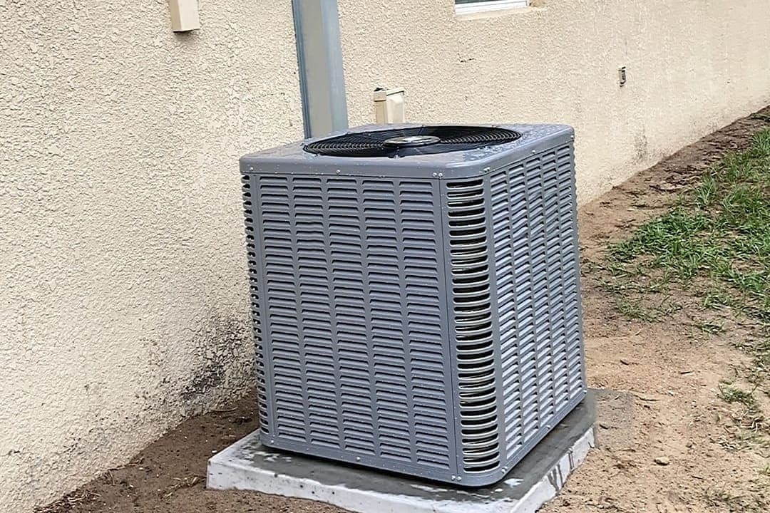 An outdoor air conditioner condenser beside a stucco house wall.