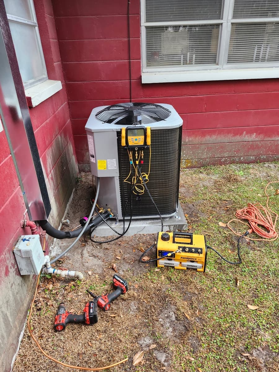 An outdoor condenser hooked up to a gauge manifold and vacuum pump during a service call.