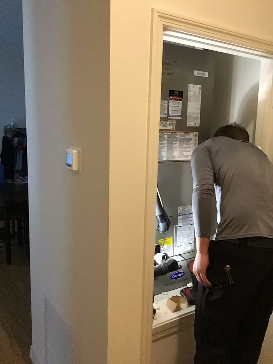 A technician servicing an air handler in a hall closet.