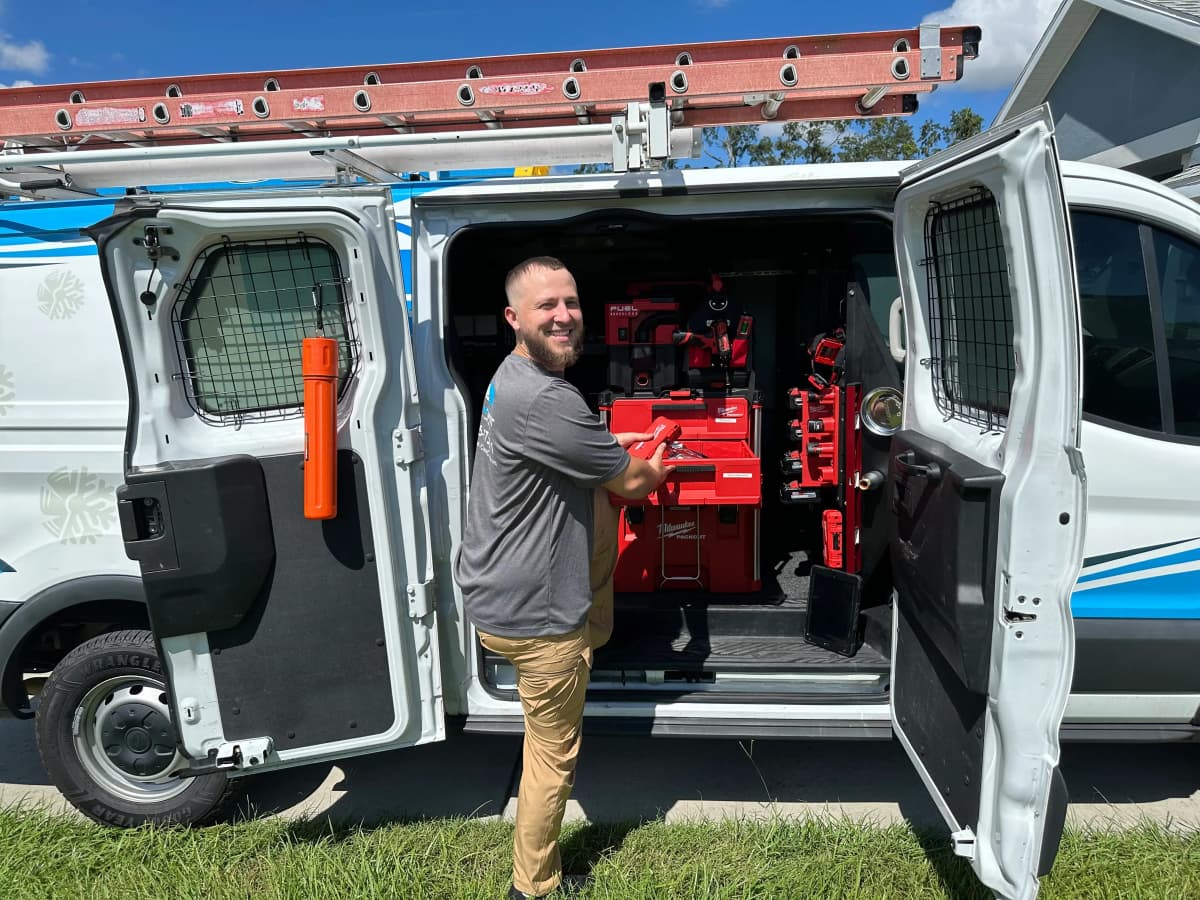 SunCoast Air Conditioning technician at the open side door of the company van, fitted out with tool storage
