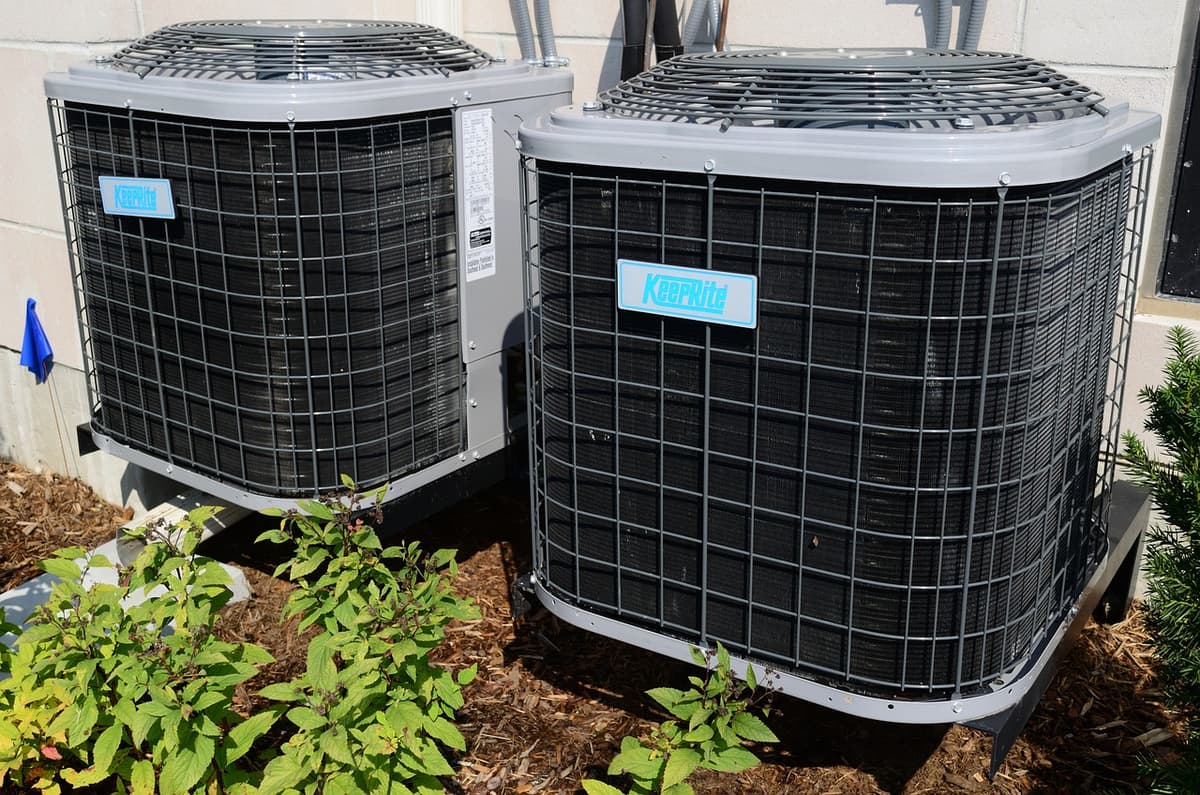 Two outdoor AC condensers on a mulched pad beside a home