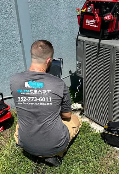 SunCoast technician kneeling at an outdoor condenser to run air conditioning diagnostics