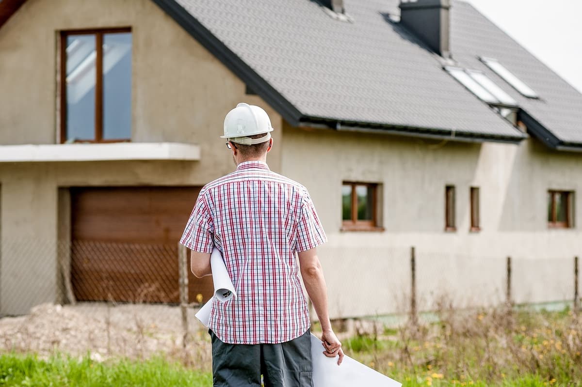 Contractor in a hard hat holding plans in front of a new home under construction
