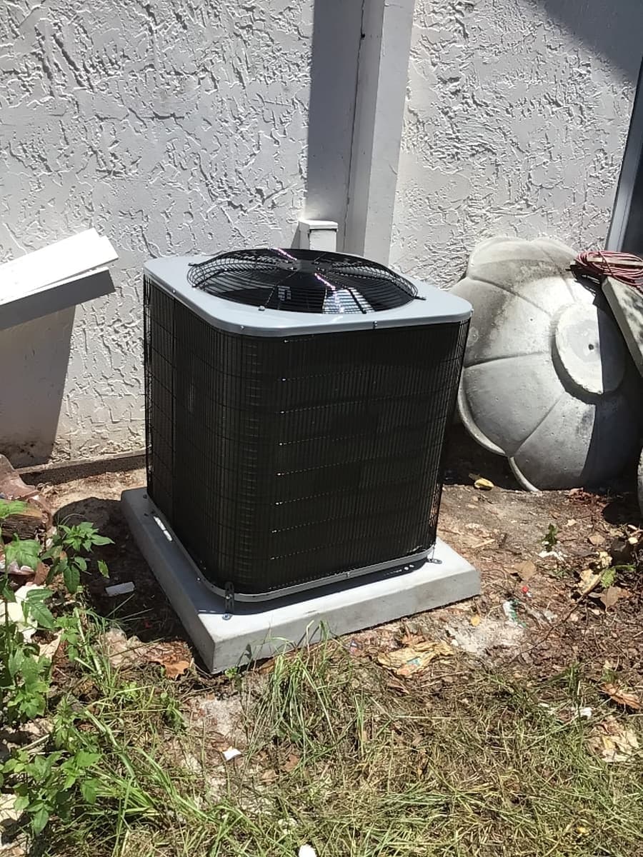 A black outdoor condenser on a pad in a side yard.
