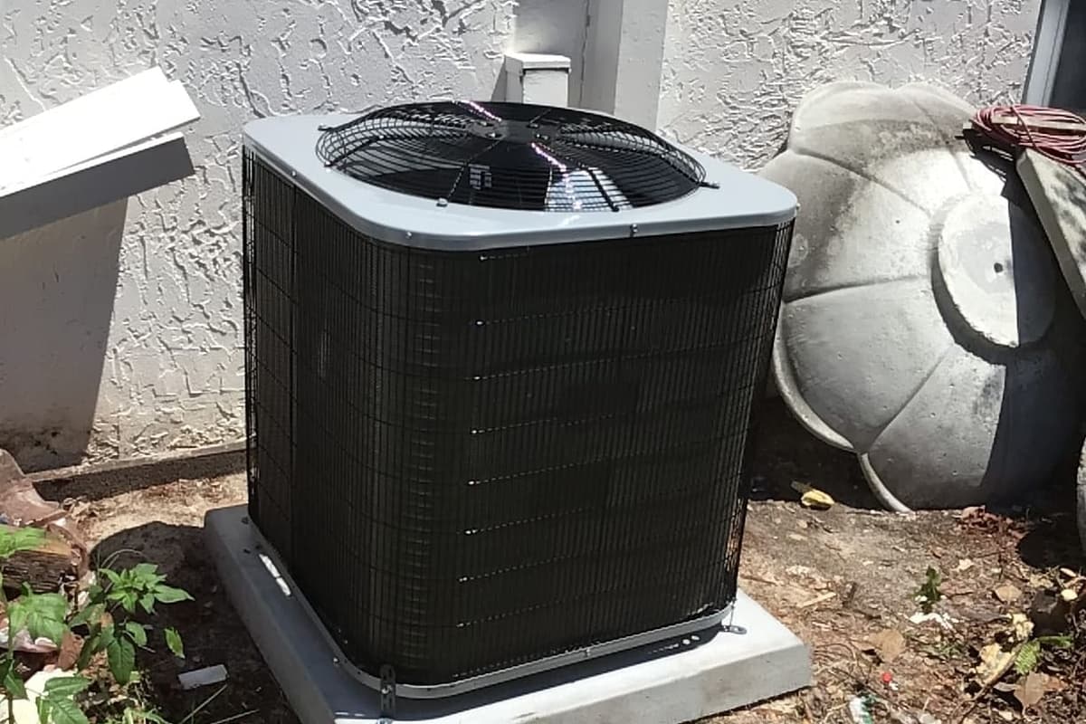 A black outdoor condenser on a pad in a side yard.