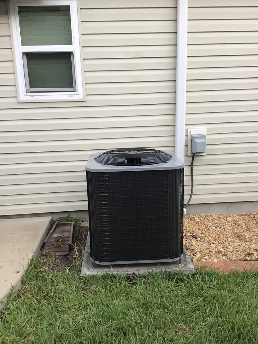A black outdoor condenser against vinyl siding with its disconnect box.