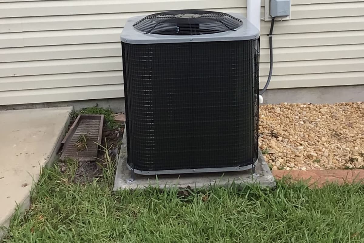 A black outdoor condenser against vinyl siding with its disconnect box.