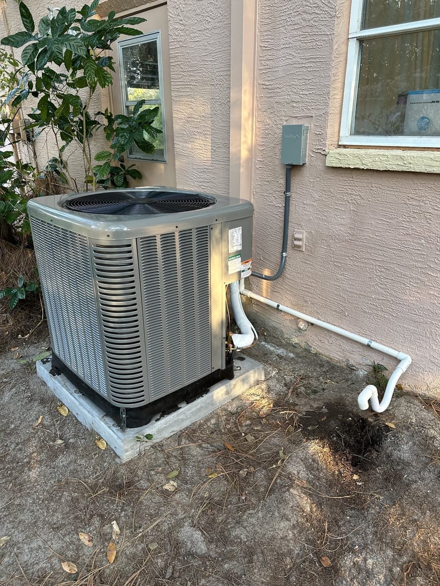A gray outdoor condenser on a composite pad beside a condensate drain line in Spring Hill, FL.
