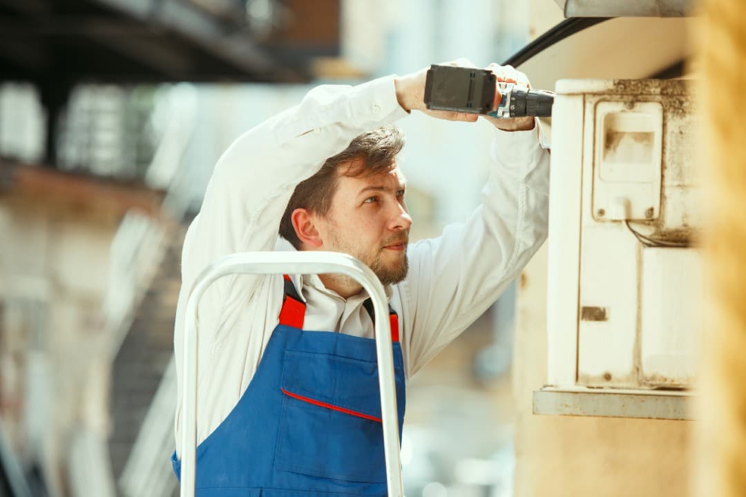 Technician on a stepladder servicing a wall-mounted unit