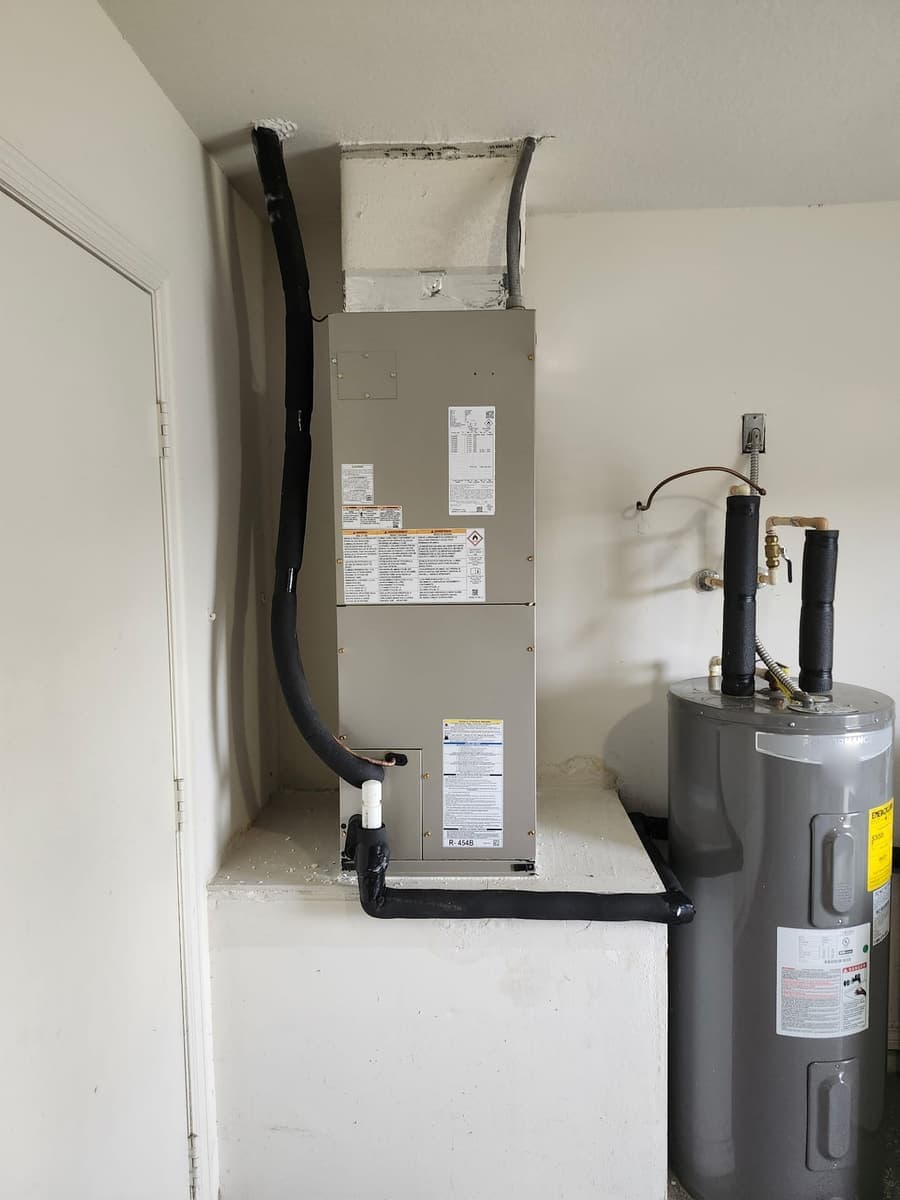 An indoor air handler with its condensate line, beside a water heater.