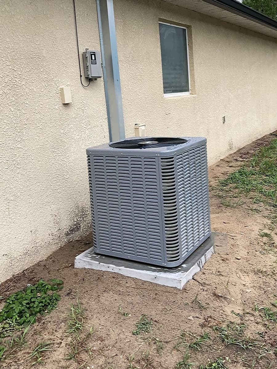 An outdoor air conditioner condenser beside a stucco house wall.