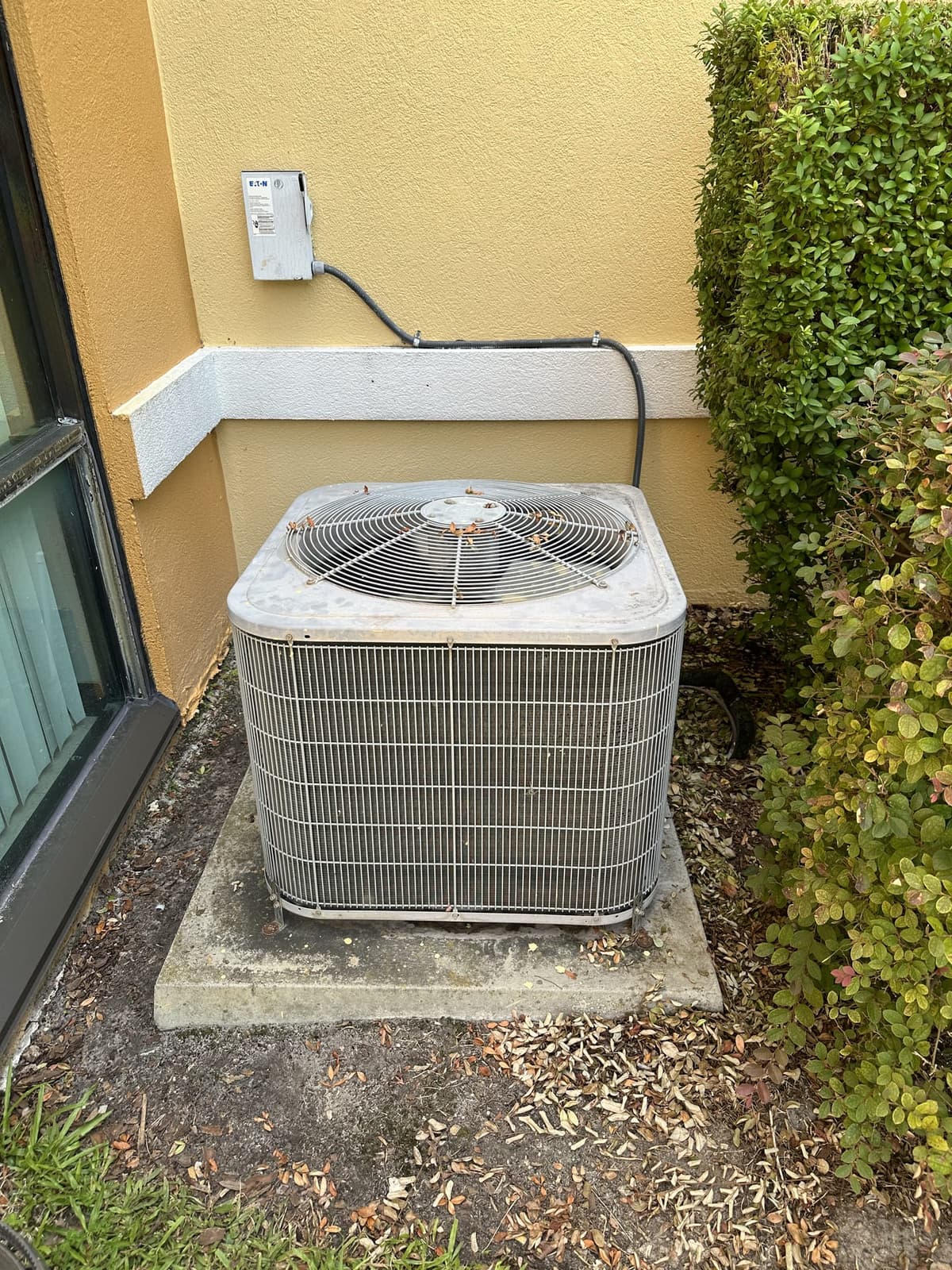 An older outdoor air conditioning condenser unit beside a home, due for inspection or replacement