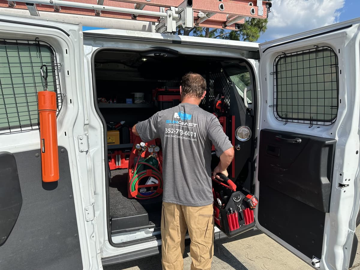 SunCoast technician kneeling to grab tools from the organised rear compartment of the service van