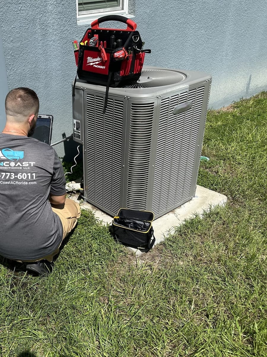 A SunCoast technician crouched at an outdoor condenser during a service visit in Spring Hill, FL.