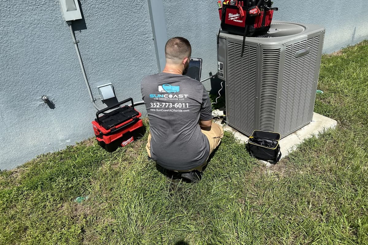 A SunCoast technician crouched at an outdoor condenser during a service visit in Spring Hill, FL.