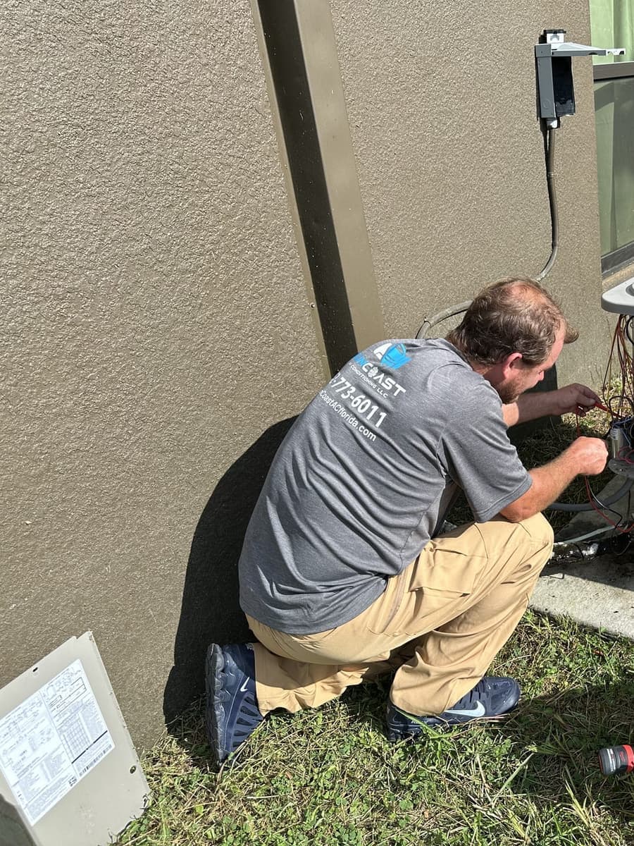 A SunCoast technician kneeling at an outdoor condenser beside a red tool bag in Spring Hill, FL.