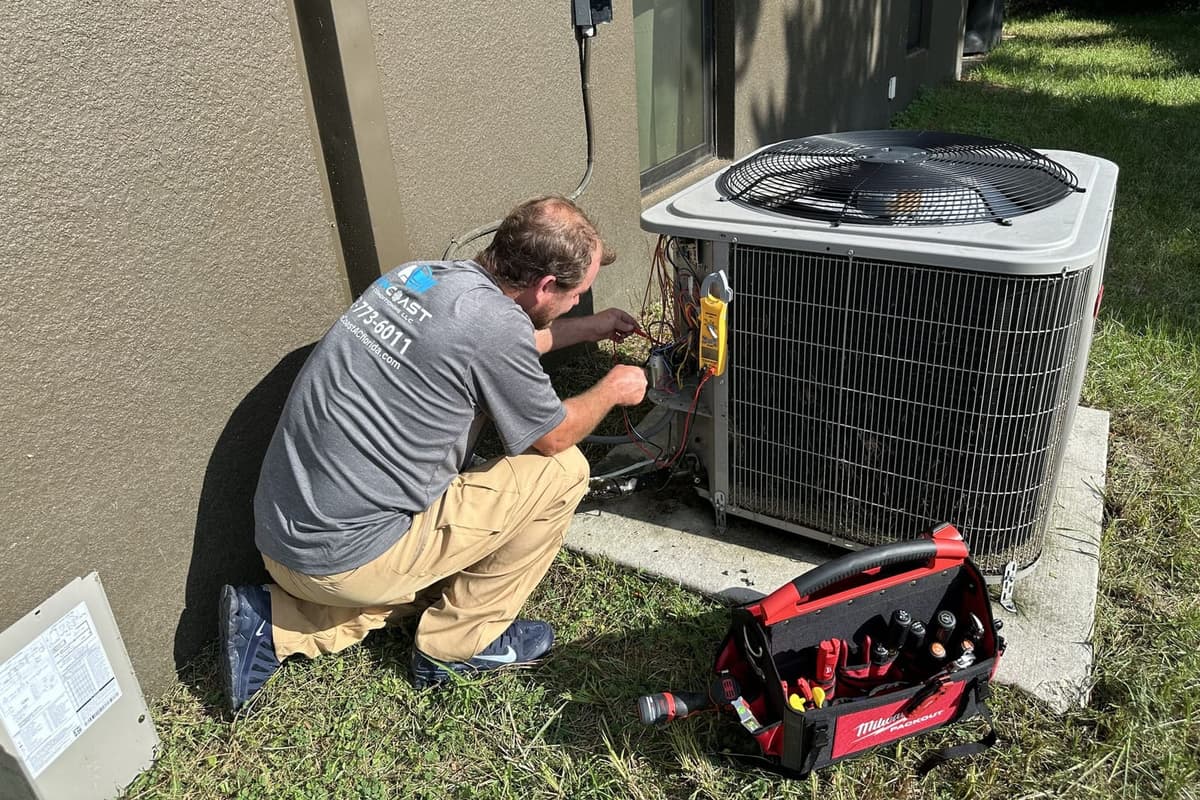 A SunCoast technician kneeling at an outdoor condenser beside a red tool bag in Spring Hill, FL.