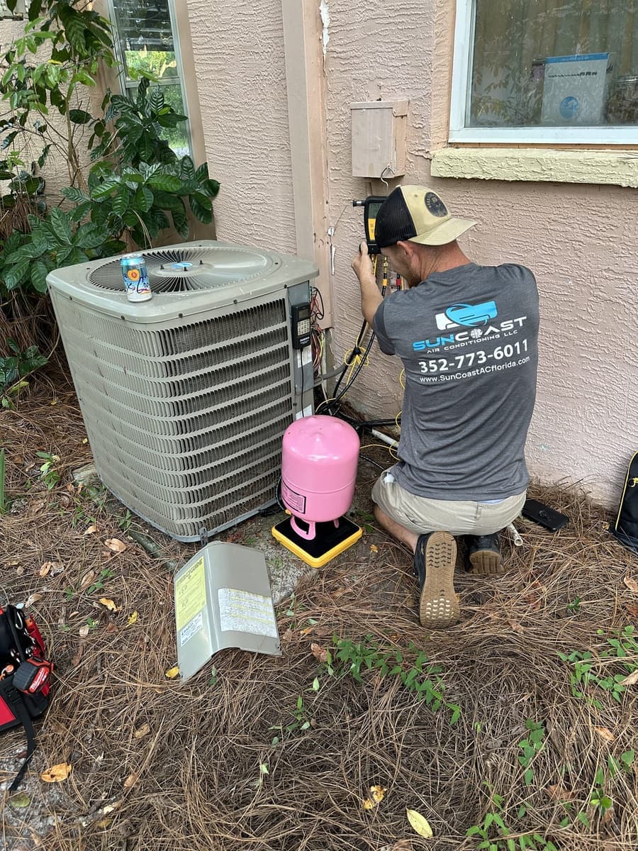 A SunCoast technician working at an outdoor condenser with a refrigerant cylinder beside him in Spring Hill, FL.