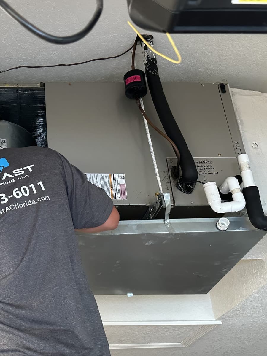 A SunCoast technician working over an air handler drain pan.