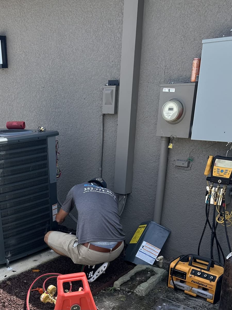 A technician kneeling at an outdoor condenser with test meters laid out on the ground in Pasco County, FL.