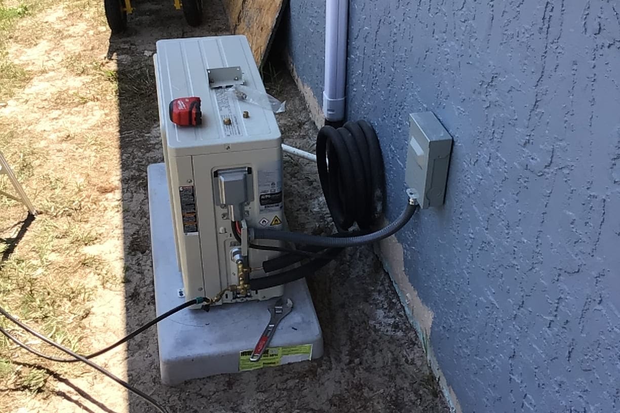 A ductless mini-split outdoor unit being set beside a stucco wall.