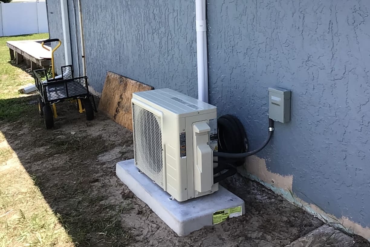 A ductless outdoor unit installed beside a fenced yard.