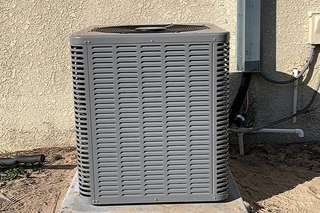 A gray outdoor condenser on a pad beside a stucco wall.