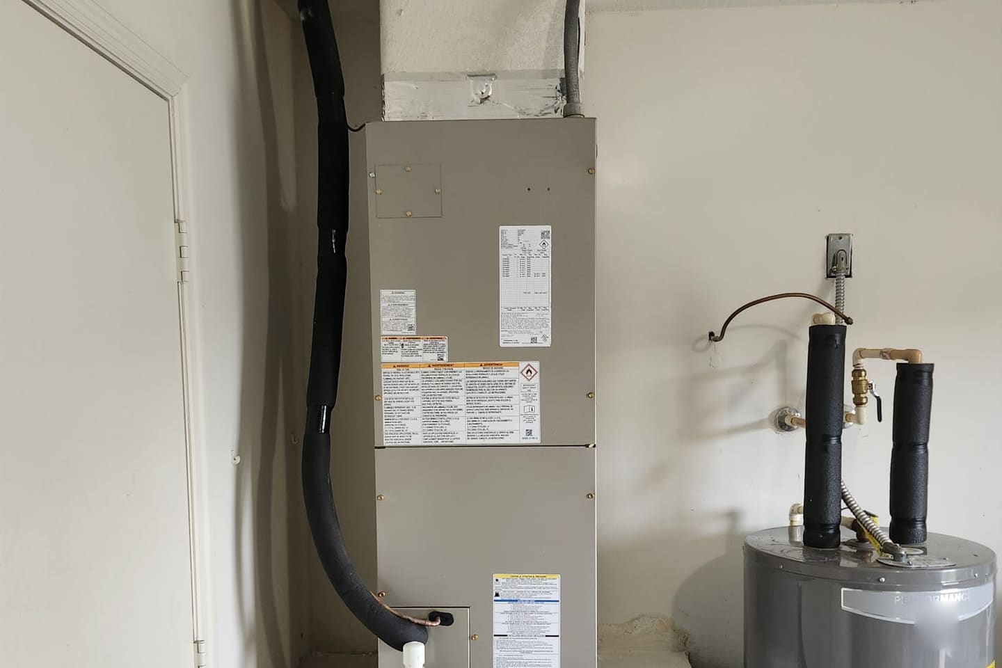 An indoor air handler with its condensate line, beside a water heater.