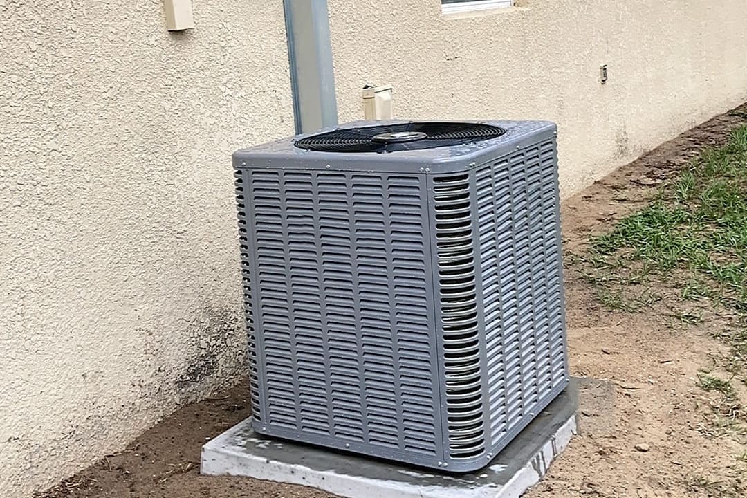 An outdoor air conditioner condenser beside a stucco house wall.