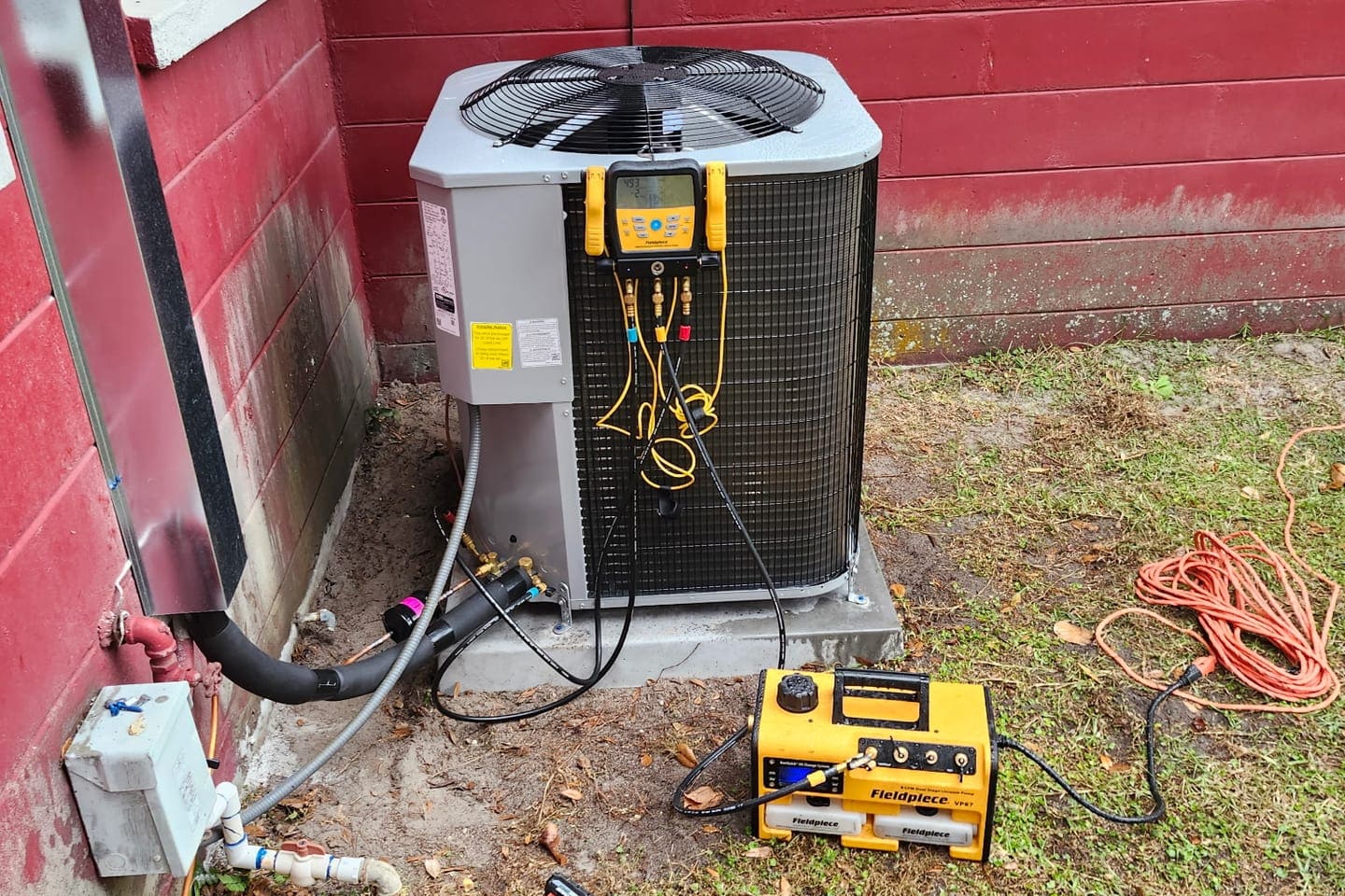 An outdoor condenser hooked up to a gauge manifold and vacuum pump during a service call.